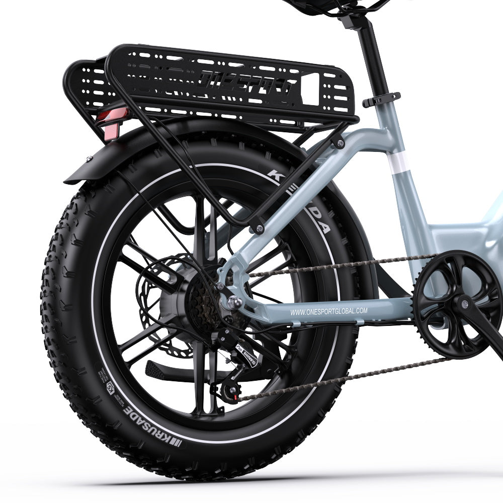 Close-up rear view of a light blue onesport OT08 electric bicycle with a black rear cargo basket, black fender, fat tire, disc brakes, and chainring, on a white studio background.