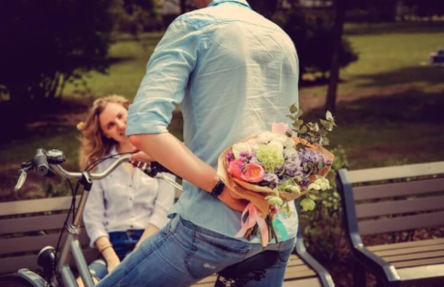 Electric bike lifestyle scene in park, man holding bouquet behind back, woman sitting on bench