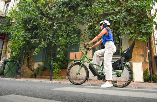 Woman riding green electric bike with cargo on city street, Pogo Cycles e-bike shop