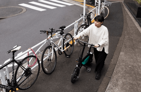 woman walking a compact electric bike with a green frame on a city sidewalk