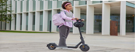 Young woman with backpack standing next to electric scooter outside modern building, Pogo Cycles