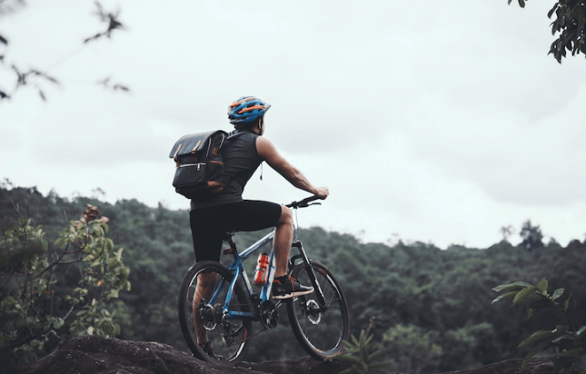 Person riding electric bike on forest trail, wearing helmet and backpack, Pogo Cycles