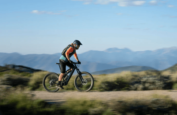 Electric mountain bike side view on trail with cyclist, scenic outdoor landscape background